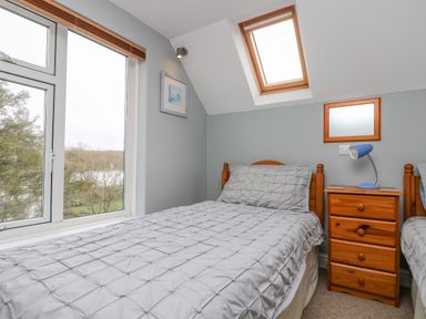 A bedroom with two single beds a wooden nightstand with a blue lamp and a large window at The Watch in Porthcurno