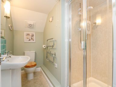 A bathroom with a toilet having a wooden seat a white sink a glass shower enclosure and a towel radiator at The Watch in Porthcurno