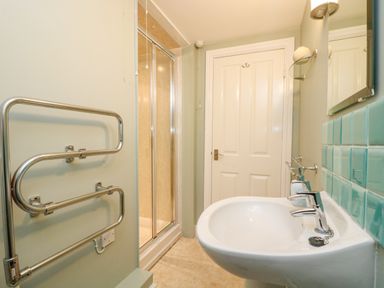 A bathroom with a white sink and two faucets a white door a glass shower enclosure and a wall-mounted towel rail at The Watch in Porthcurno