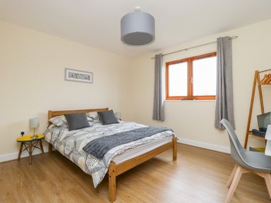 A bedroom with a wooden bed a small yellow table a grey chair and a window with curtains at Oak Lodge in Sheriff Hutton