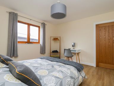 A bedroom with a bed with patterned bedding a wooden door a window with curtains a small desk and chair at Oak Lodge in Sheriff Hutton