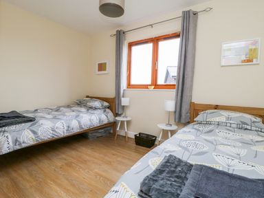 A bedroom with two single beds side tables with lamps and a window with curtains at Oak Lodge in Sheriff Hutton