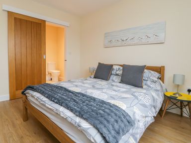 A bedroom with a wooden bed and patterned bedding next to a small yellow side table and an open door to a bathroom at Oak Lodge in Sheriff Hutton