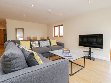 A living room with grey sofas yellow patterned cushions a coffee table with board games and a flat-screen TV on a stand at Oak Lodge in Sheriff Hutton