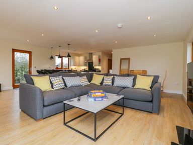 A living room with a gray sectional sofa and patterned cushions a coffee table and a kitchen in the background at Oak Lodge in Sheriff Hutton