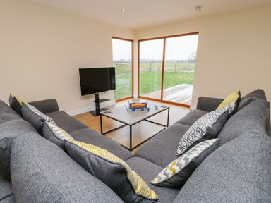 A living room with grey sofas and a coffee table in front of large windows at Oak Lodge in Sheriff Hutton