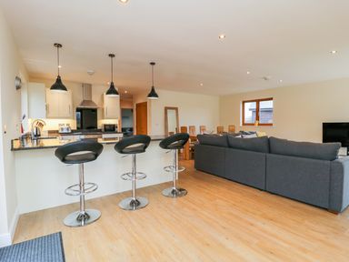 An open plan kitchen and living room with bar stools a dining table and a grey sofa at Oak Lodge in Sheriff Hutton