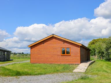 A wooden cabin with a single window and a concrete pathway surrounded by grass at Oak Lodge in Sheriff Hutton