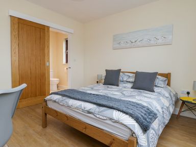 A bedroom with a wooden bed and patterned bedding a sliding wooden door leading to a bathroom with a toilet and a small table with a lamp at Rose Lodge in Sheriff Hutton