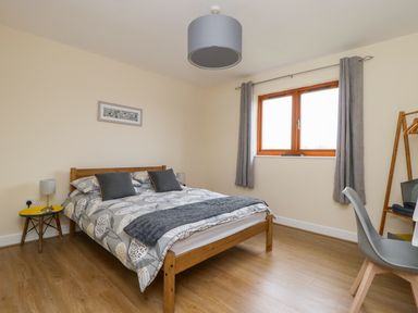 A bedroom with a wooden bed a bedside table two lamps a window with curtains and a chair at Rose Lodge in Sheriff Hutton