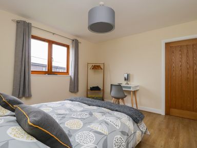 A bedroom with a bed a window with curtains a wooden door a small desk with a chair and a clothes rack at Rose Lodge in Sheriff Hutton
