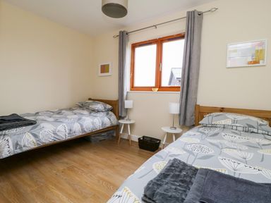 A bedroom with two single beds each with patterned bedding two white bedside tables with lamps a window with grey curtains and wooden floor at Rose Lodge Sheriff Hutton