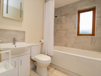 A bathroom with a sink vanity toilet bathtub shower curtain and a window at Rose Lodge in Sheriff Hutton
