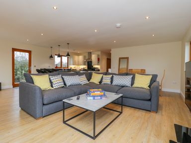 A living room with a grey sectional sofa with patterned cushions a coffee table and an open kitchen at Rose Lodge in Sheriff Hutton