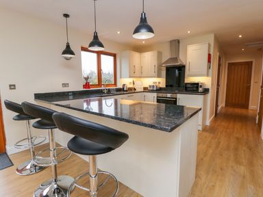 A kitchen with black countertop bar stools and hanging lights at Rose Lodge in Sheriff Hutton