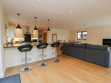 An open plan kitchen and living room with bar stools a sofa and dining table at Rose Lodge in Sheriff Hutton
