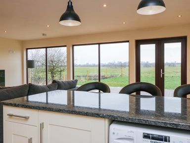 A kitchen island with black countertop and stools looking out to large windows and glass doors with a view of a green field at Rose Lodge in Sheriff Hutton