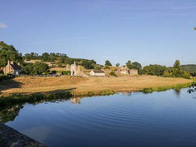 A landscape with a river in the foreground and ruins and houses on a hill at Rose Lodge in Sheriff Hutton