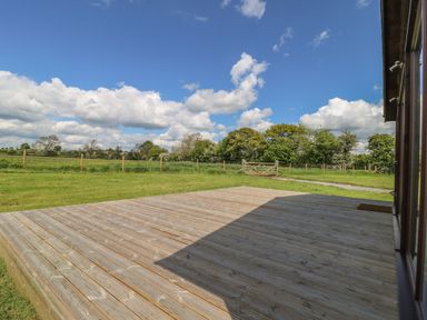 An outdoor wooden deck overlooking a grassy field with a wooden fence and gate under a blue sky at Rose Lodge in Sheriff Hutton