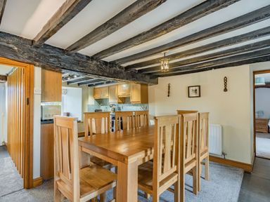 A dining area with a wooden table and six chairs next to a kitchen with wooden cabinets at Gwrtheyrn in Dyffryn Ardudwy