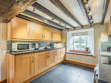 A kitchen with wooden cabinets a microwave kettle toaster and a window seat at Gwrtheyrn in Dyffryn Ardudwy
