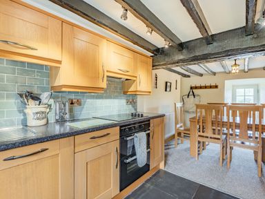 A kitchen with wooden cabinets and a black oven next to a dining area with wooden chairs at Gwrtheyrn in Dyffryn Ardudwy