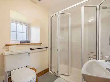 A bathroom with a toilet towel on windowsill shower with folding glass door and a sink at Gwrtheyrn in Dyffryn Ardudwy
