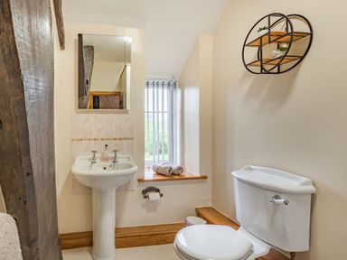 A bathroom with a pedestal sink a toilet a small window with towels and a circular wall shelf at Gwrtheyrn in Dyffryn Ardudwy
