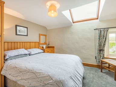 A bedroom with a double bed wooden headboard wooden bedside table and a window with floral curtains at Gwrtheyrn in Dyffryn Ardudwy