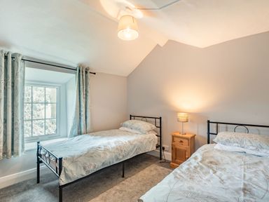 A bedroom with two single beds a wooden nightstand and a window with curtains at Gwrtheyrn in Dyffryn Ardudwy
