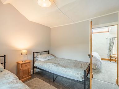 A bedroom with two single beds one with floral bedding and a wooden nightstand with a lamp at Gwrtheyrn in Dyffryn Ardudwy