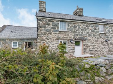 Stone cottage with slate roof surrounded by greenery and stone wall at Gwrtheyrn in Dyffryn Ardudwy