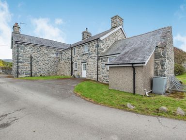 Exterior view of a stone house with a driveway and grass areas at Gwrtheyrn in Dyffryn Ardudwy