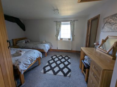 A bedroom with two single beds a window with curtains a wooden chest of drawers and a mirror at Gwrtheyrn in Dyffryn Ardudwy
