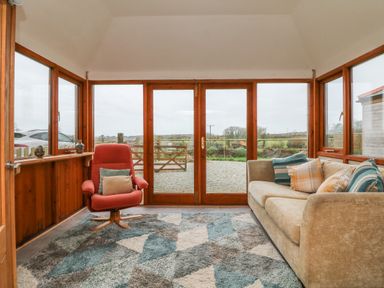 A sunroom with a beige sofa and a red armchair on a patterned rug at Edwin's View in Nancegollan nr Porthleven