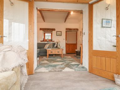 A sitting room with a couch a wooden coffee table and a rug seen through wooden framed glass doors at Edwin's View in Nancegollan nr Porthleven