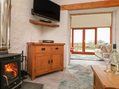 A living area with a wood burning stove wooden cabinet and television opening to a sitting area with sofa and glass doors at Edwin's View in Nancegollan nr Porthleven