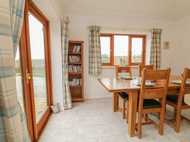 A dining room with a wooden table and chairs near windows and a glass door with curtains at Edwin's View in Nancegollan nr Porthleven
