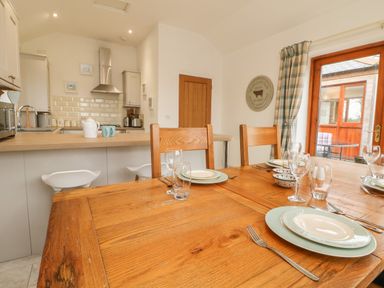 A dining table set with plates glasses and cutlery next to a kitchen with stools and wooden door at Edwin's View in Nancegollan nr Porthleven
