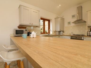 A kitchen with wooden countertop stools a microwave kettle sink and gas stove at Edwin's View in Nancegollan nr Porthleven