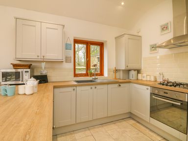 A kitchen with white cabinets wooden countertop a window above the sink and appliances at Edwin's View in Nancegollan nr Porthleven