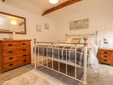 A bedroom with a metal bed frame a wooden dresser and side table with lamps and floral art on the walls at Edwin's View in Nancegollan nr Porthleven