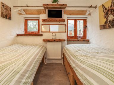 A bedroom with two single beds striped bedding a small wall-mounted tv and two windows at Edwins View in Nancegollan nr Porthleven