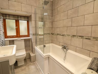 A bathroom with a bathtub a glass shower screen a toilet a sink and a window with a checked blind at Edwin's View in Nancegollan nr Porthleven