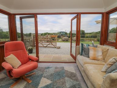A seating area with a beige sofa and orange armchair next to open glass doors overlooking a garden and field at Edwins View in Nancegollan nr Porthleven