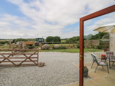 A garden patio with chairs and an umbrella overlooking a gravel driveway and a wooden gate with a tractor and fields beyond at Edwin's View in Nancegollan nr Porthleven