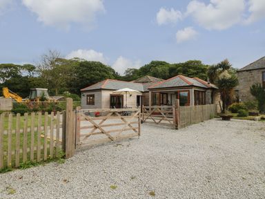 A gravel driveway with wooden gates leading to a house with multiple roof sections and outdoor seating and umbrella at Edwin's View in Nancegollan nr Porthleven