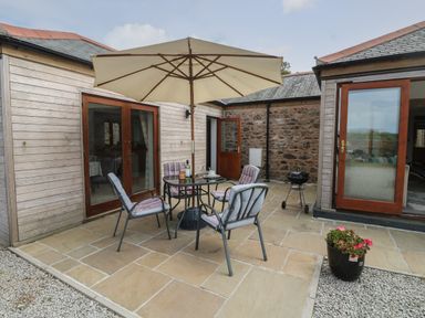 An outdoor patio area with a table and four cushioned chairs under a large umbrella outside a building at Edwin's View in Nancegollan nr Porthleven