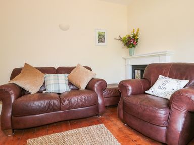A living room with brown leather sofas with cushions wooden floor a rug and a fireplace with flowers at School House in Builth Wells