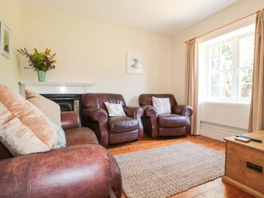 A living room with leather armchairs wooden floor a rug a window with curtains and a wooden chest at School House in Builth Wells
